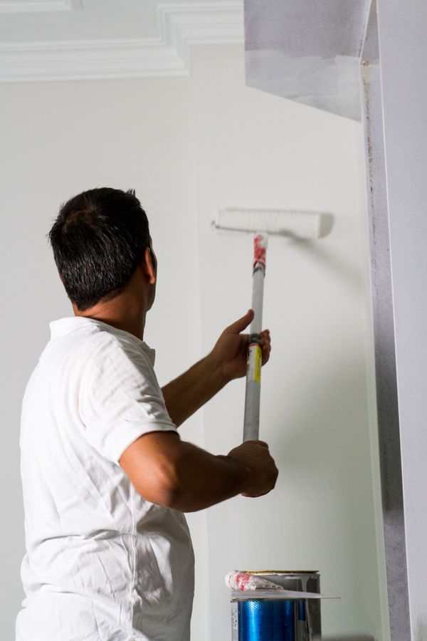 Man painting a white wall with a paint roller.