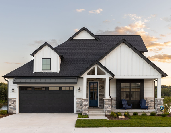 White farmhouse with black accents, black garage door, and stone accents.