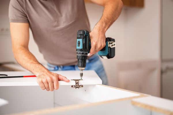 Person using a drill to install a cabinet hinge.