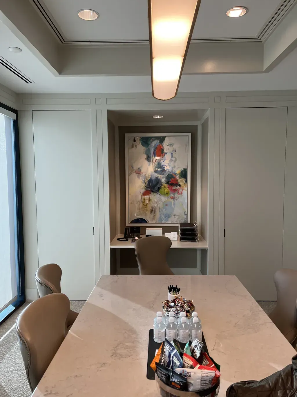A modern conference room featuring a long table with drinks, snacks, and chairs facing an abstract painting on the wall.