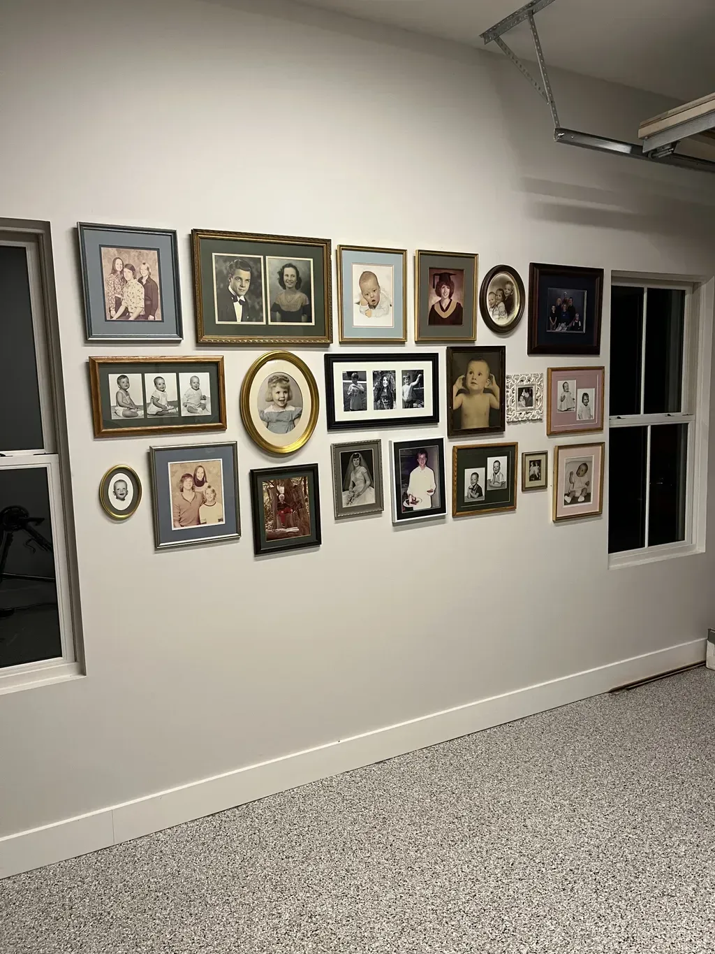 A large gallery wall featuring various framed photographs displayed on a light-colored wall above a speckled garage floor.