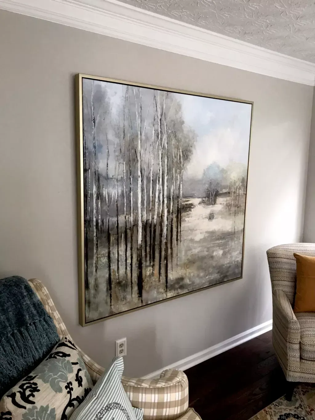A large, framed painting of birch trees in a muted, neutral landscape hangs on a light gray wall between two armchairs.