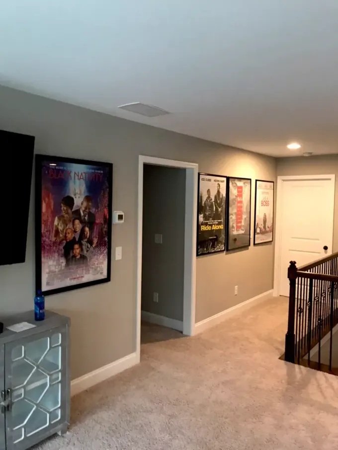 A wall featuring four framed movie posters leading to an open doorway and a staircase in a carpeted home interior.