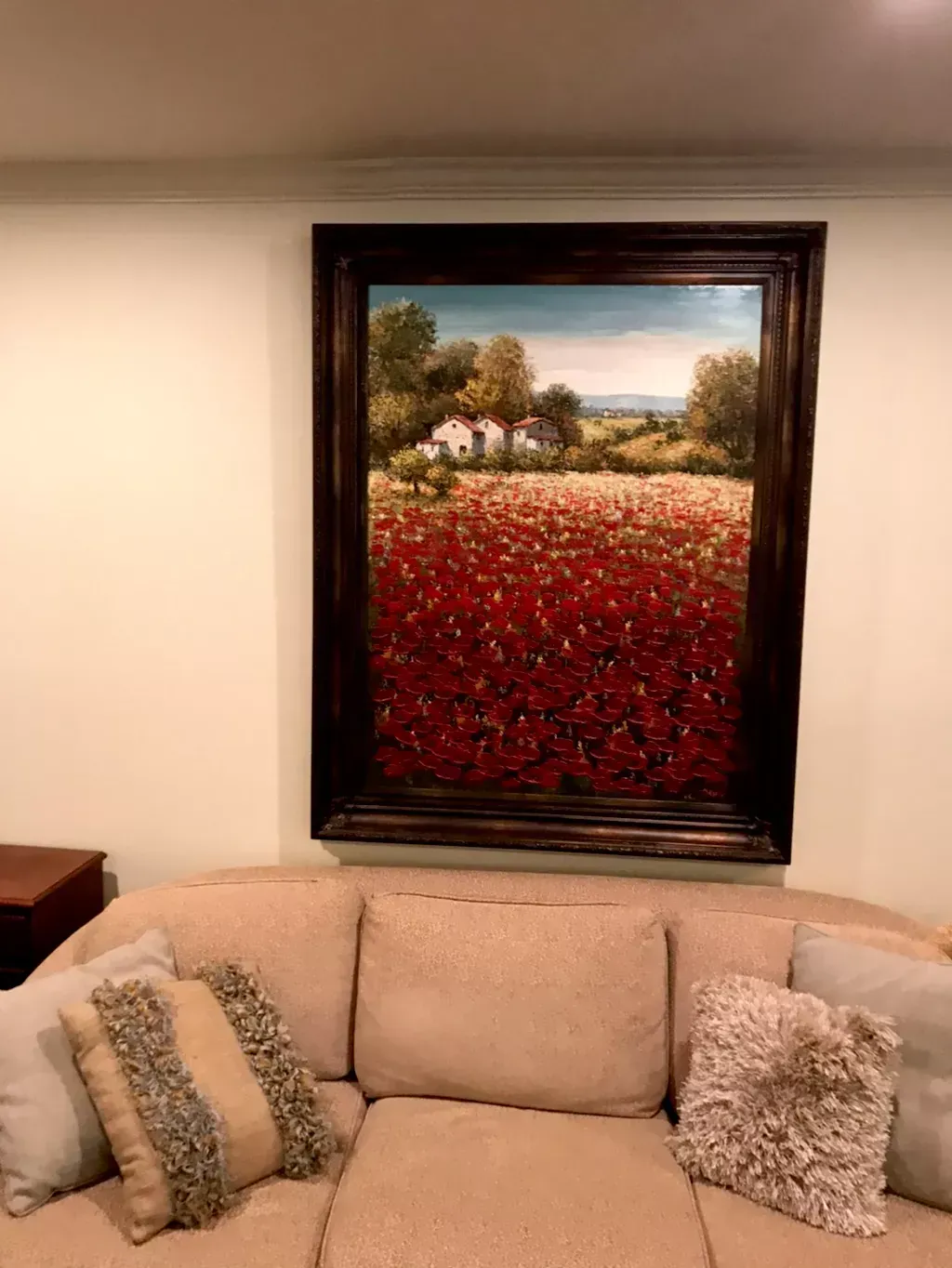 A large framed landscape painting of a vibrant red poppy field and small cottages hangs above a beige sofa.