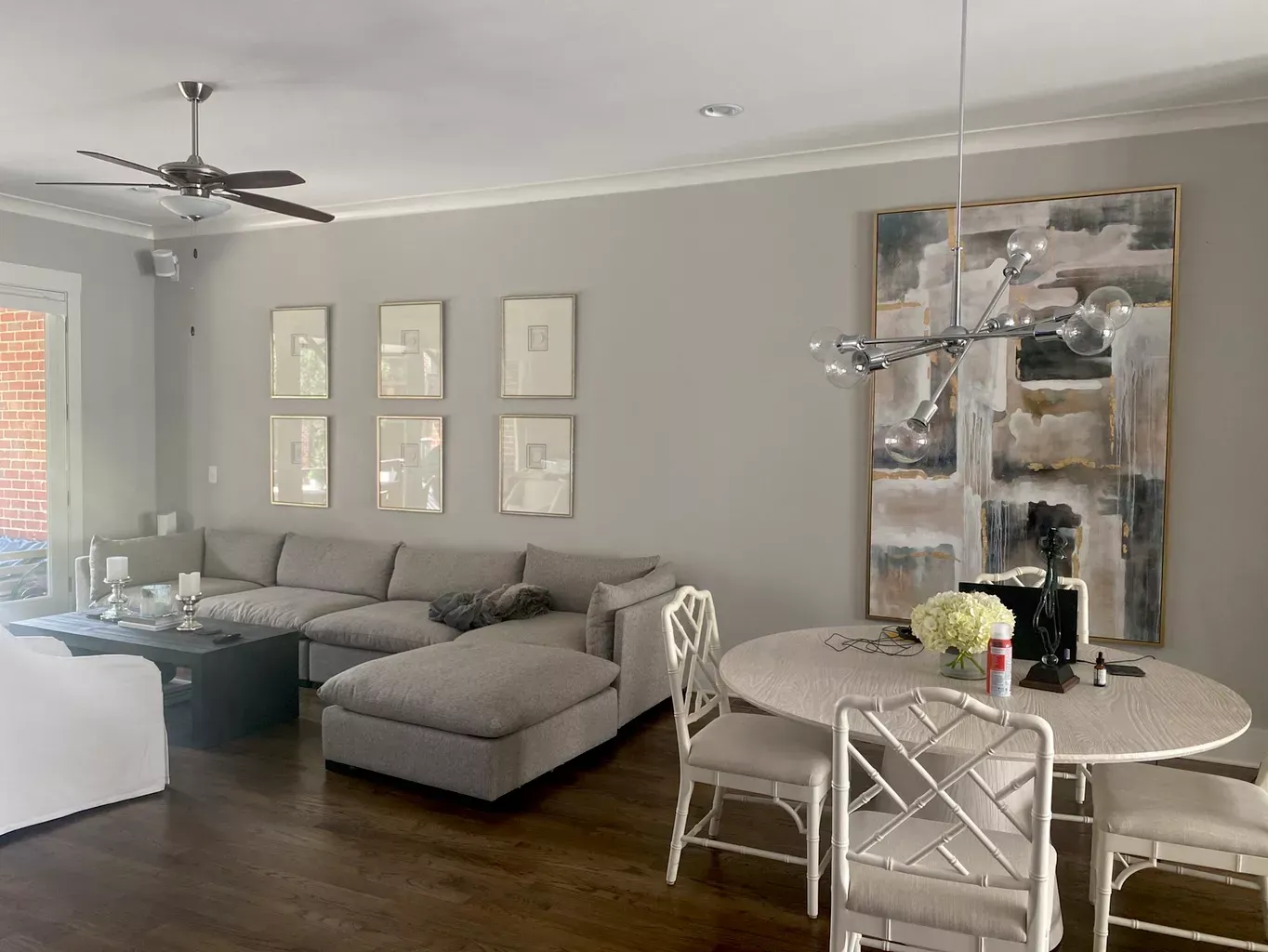An open-plan living and dining room with a grey sectional sofa, a white dining table, and large abstract wall art.