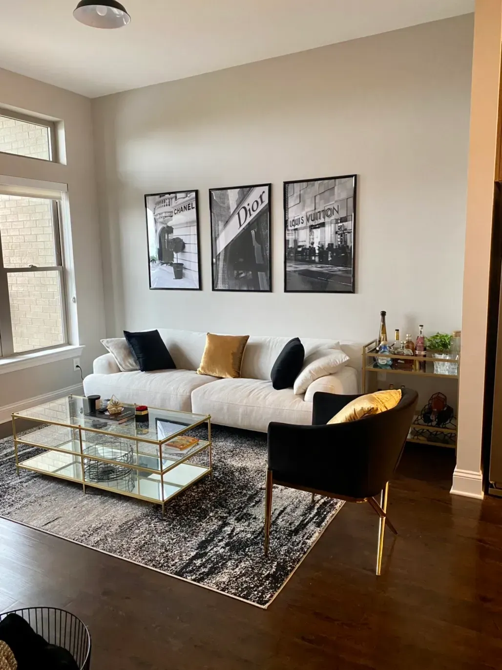 A living room with a white sofa, a black armchair, a glass coffee table, and three framed black and white art prints.
