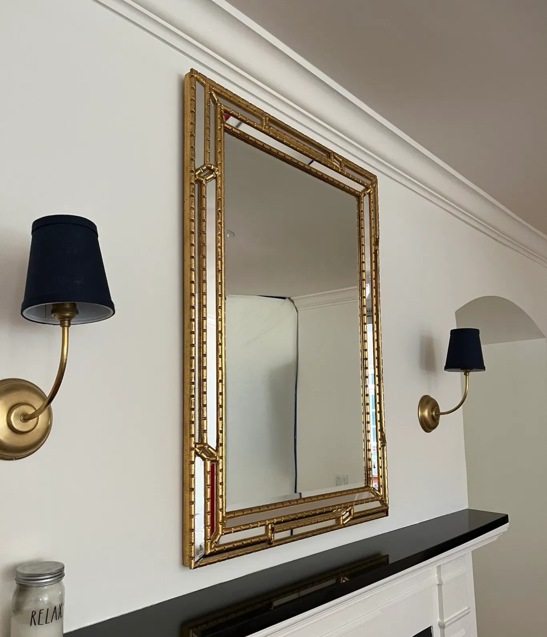 A rectangular gold mirror with a decorative frame hangs on a white wall between two navy blue wall-mounted lamps.