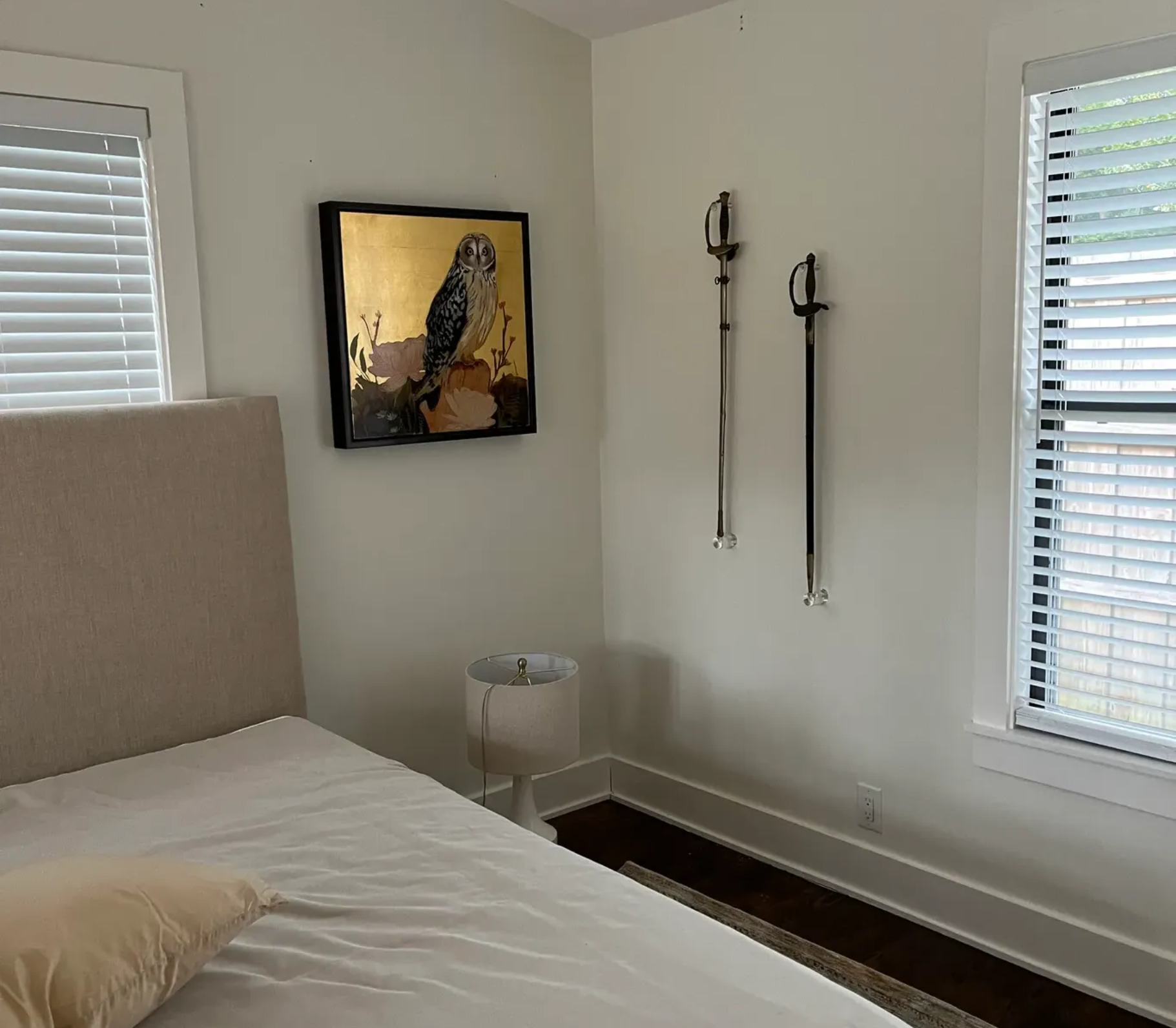 A bedroom wall featuring two mounted swords displayed horizontally below a small, gold-toned framed artwork.