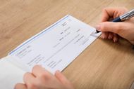 Hands holding a pen and writing on a blank company check resting on a wooden desk.
