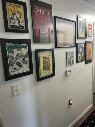 A gallery wall featuring a collection of framed vintage posters and art prints in black frames against a white wall.
