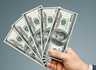 A hand holds a fanned-out stack of four US 100-dollar bills against a plain gray background.