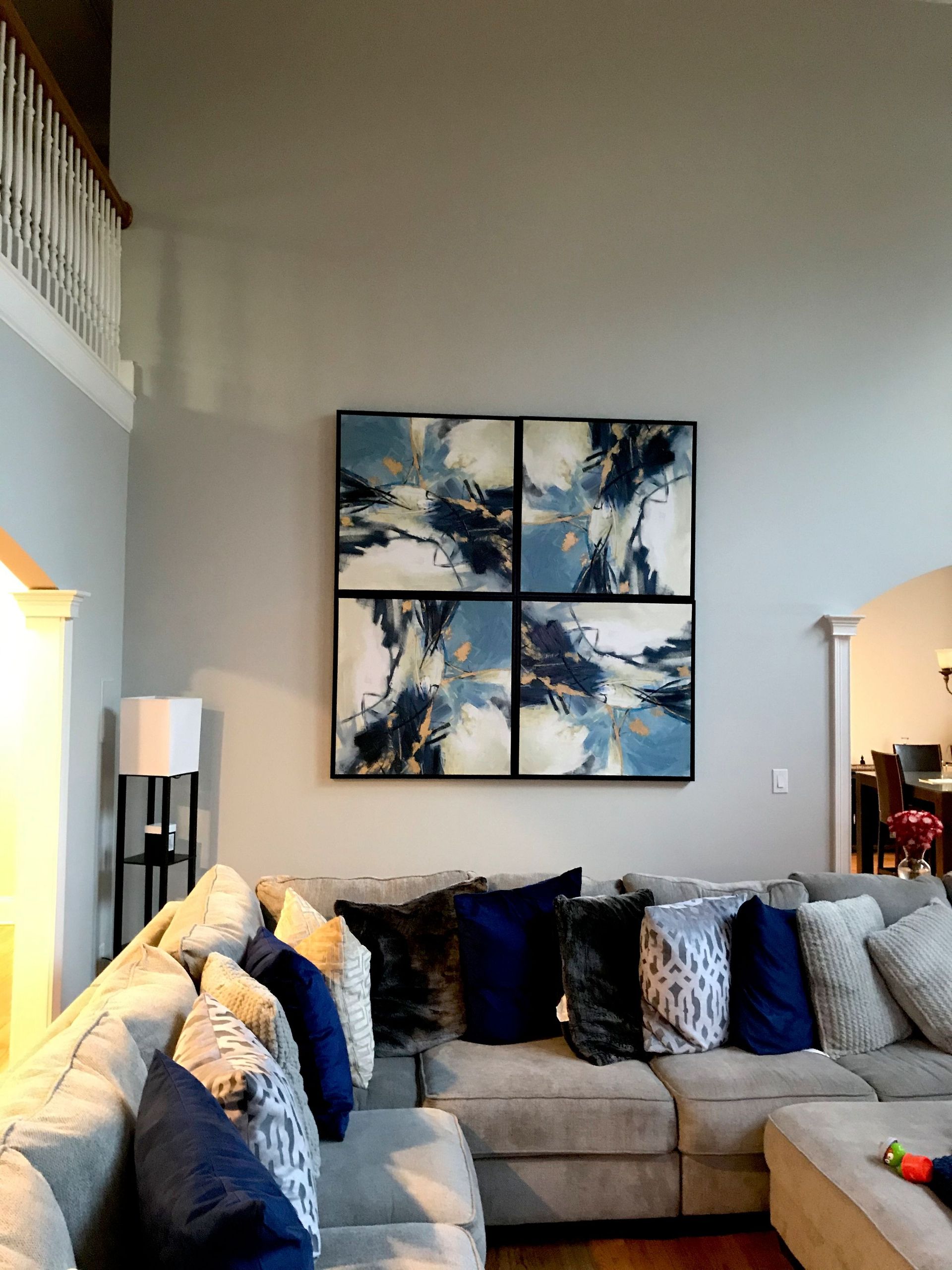 A grey living room features a sectional sofa and a large, four-paneled abstract art piece with blue and white tones.