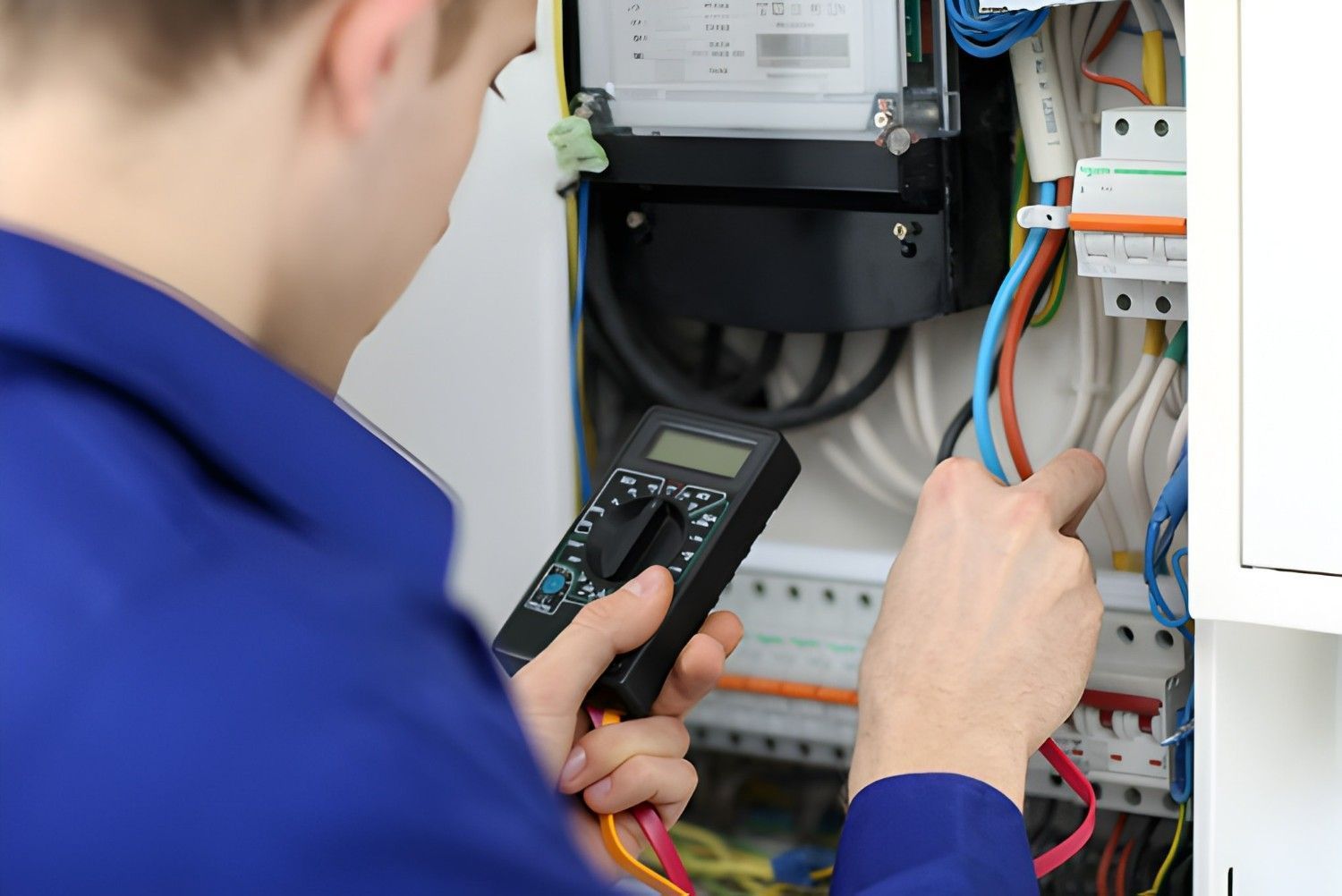 Electrician in Blue Overalls Testing Electrical Wiring in Control Panel With Multimeter — Careda Air in Saint Georges Basin, NSW