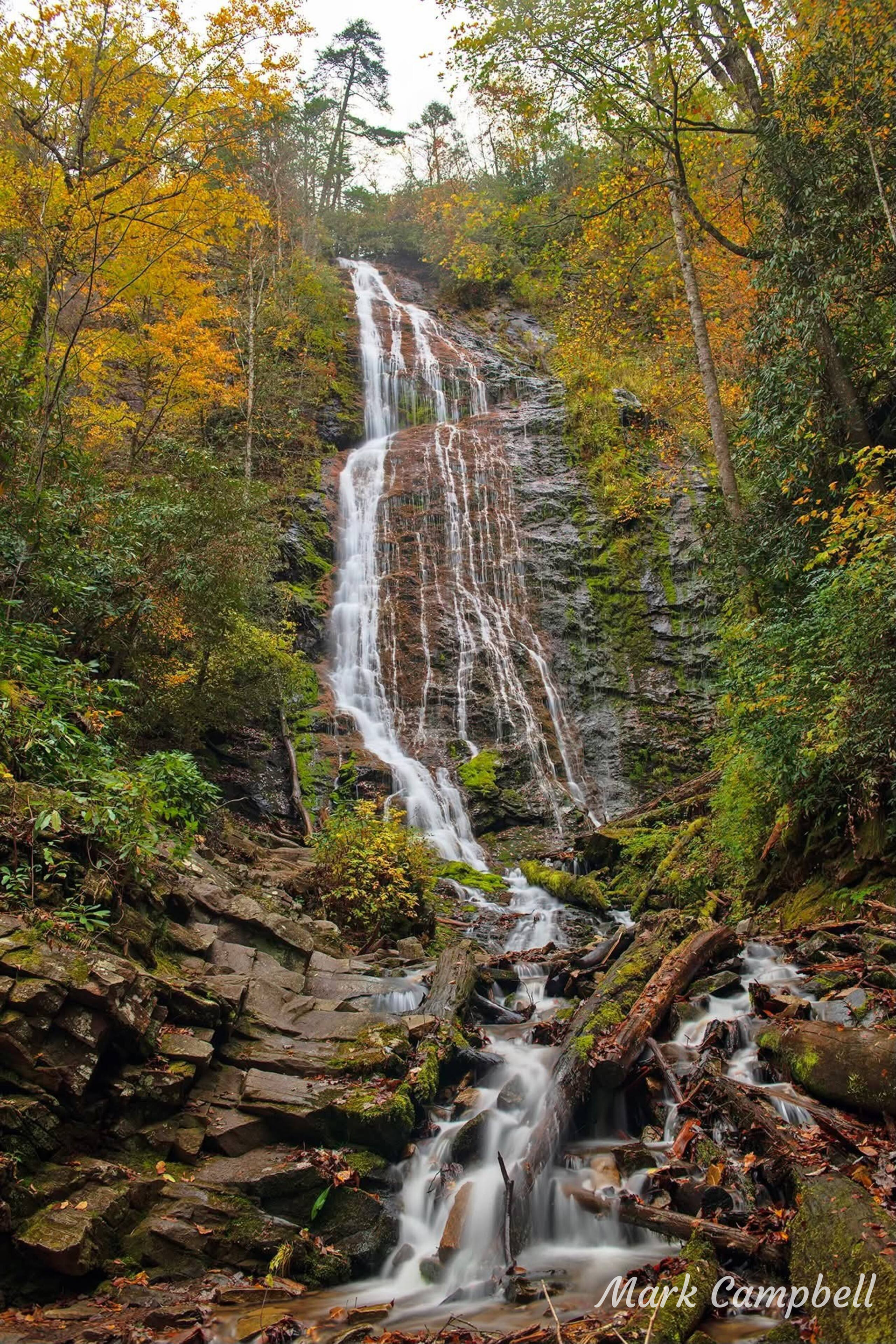 Waterfall cascading down rocky cliffside, surrounded by fall foliage.
