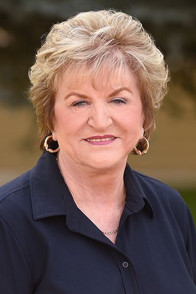 A woman wearing glasses and a blue shirt is smiling for the camera.