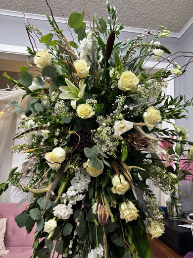 White floral funeral wreaths and bouquets displayed on stands in a dim indoor memorial setting