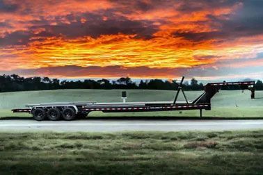 Flatbed trailer on a road with a vibrant orange and yellow sunset in the background.