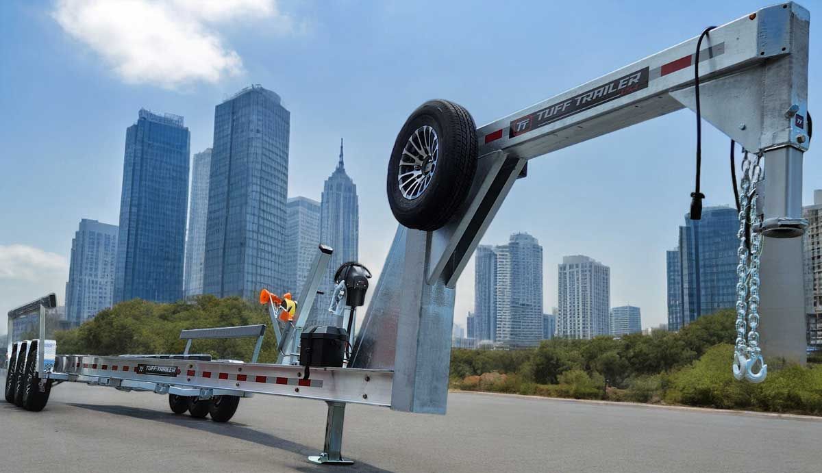 A silver tow truck with a boom, tire, and hook, against a city skyline.