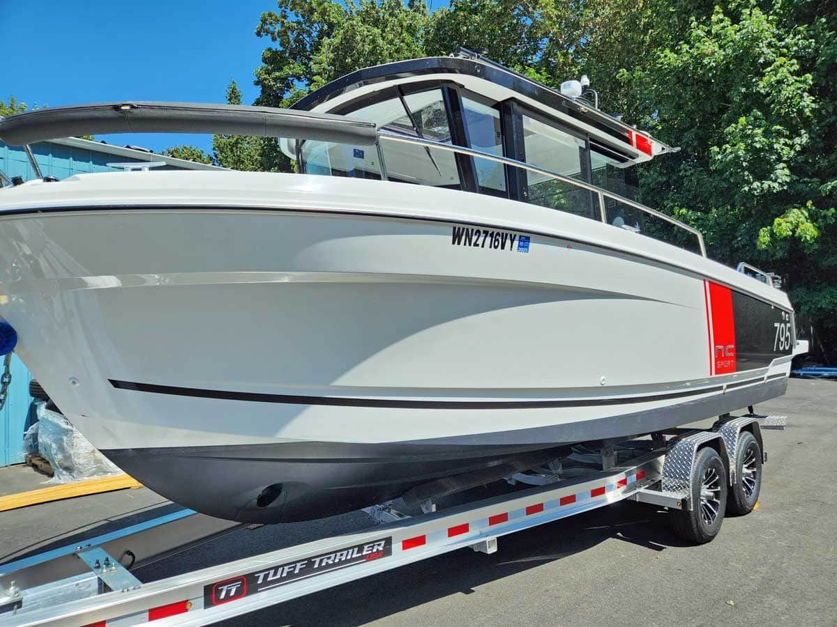 White boat on trailer, red stripe, black trim, parked outside.