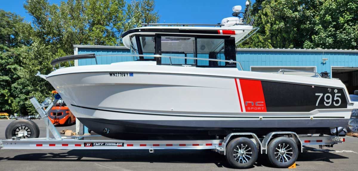 A white and gray boat on a trailer, with a red stripe and black accents, parked outside a building.