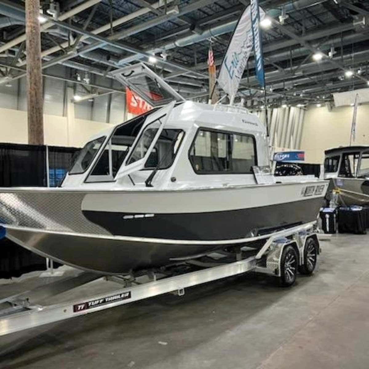 Aluminum boat on a trailer at a boat show, white cabin, gray hull.