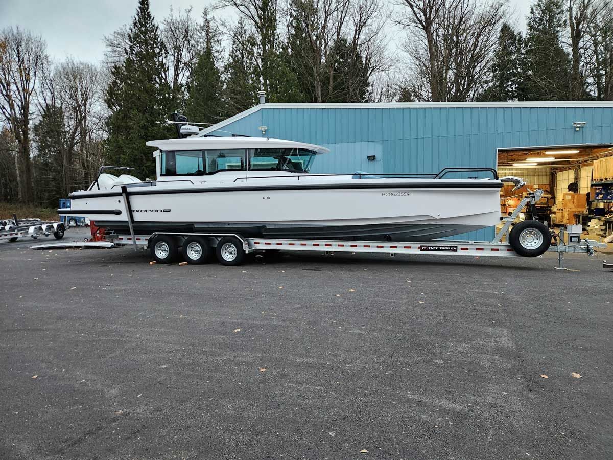 White boat on a trailer in front of a blue building with trees in the background.