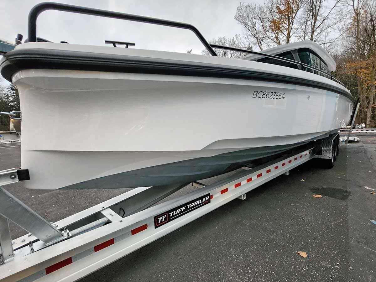 White motorboat on a trailer, parked on asphalt. Black railing on top, gray hull.