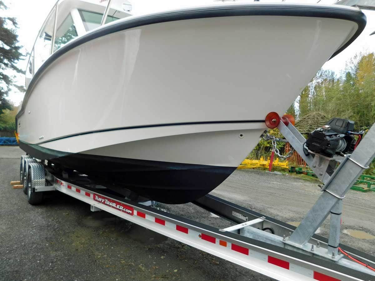 White motorboat on a trailer, outside, with trees in background.
