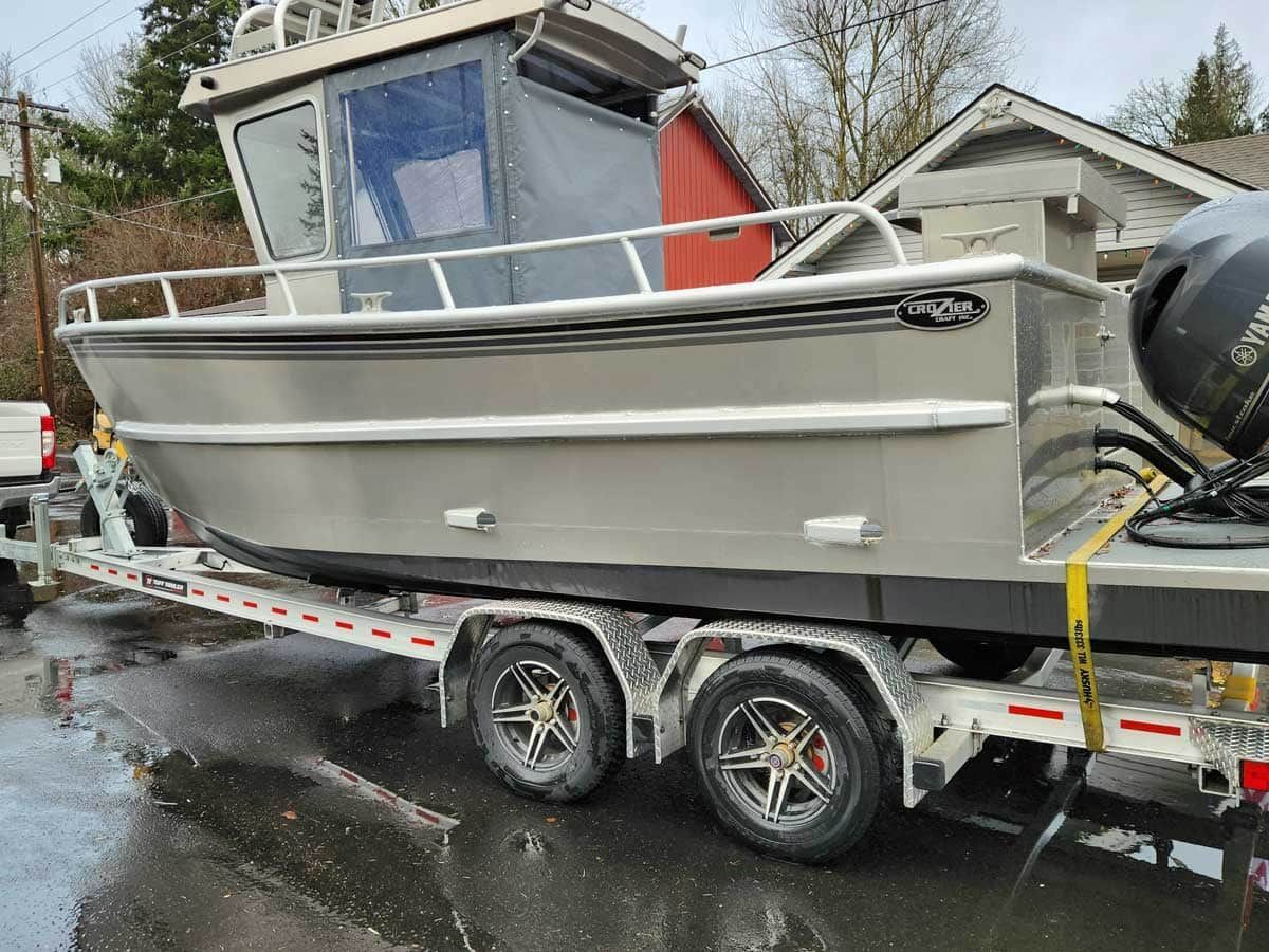 Silver boat on a trailer, parked on a wet street.
