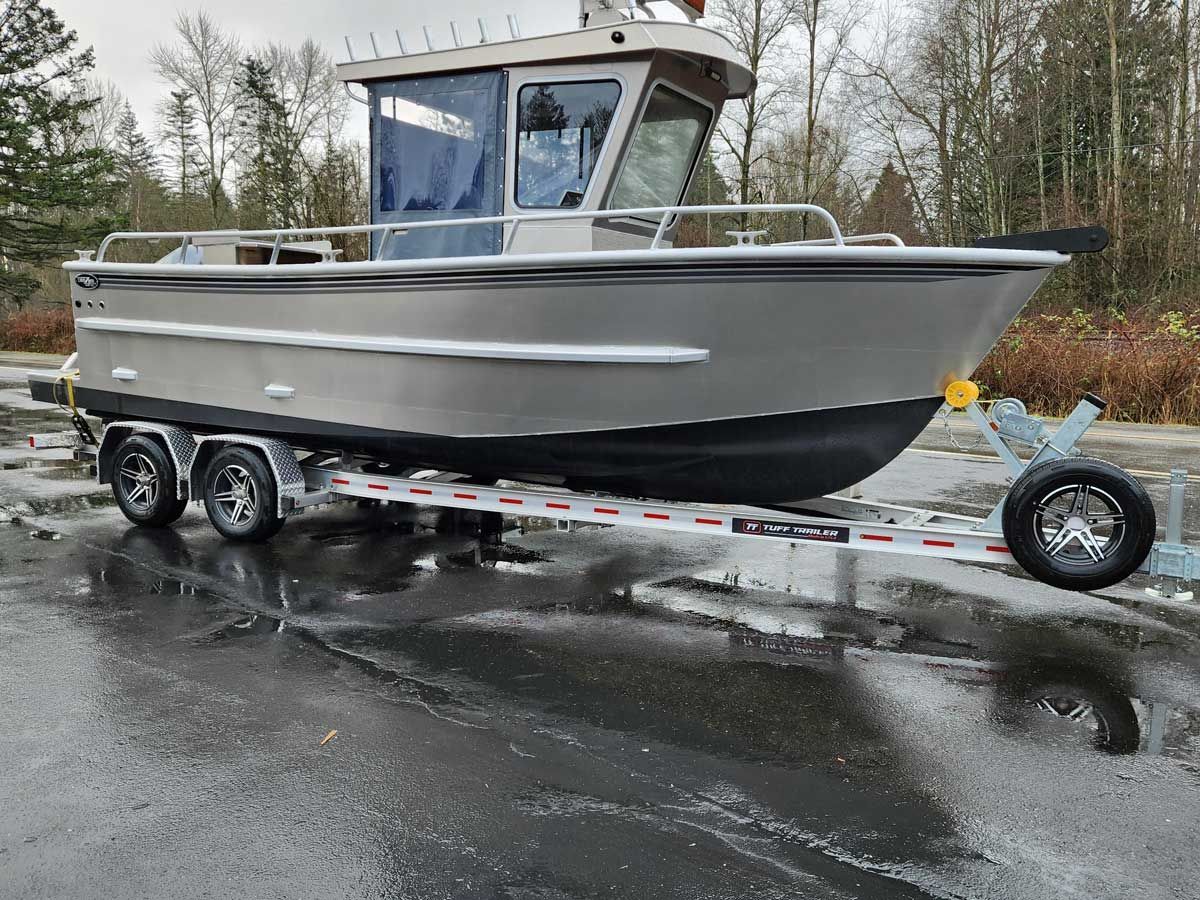 Silver aluminum boat on a trailer, parked on a wet asphalt surface, overcast sky in the background.