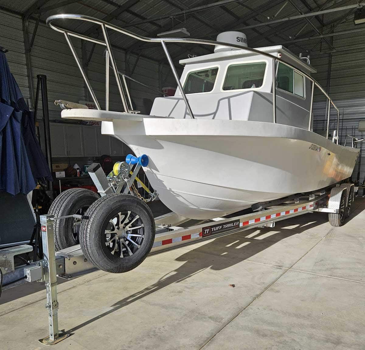 White boat on a trailer inside a building with a metal frame and tires visible.