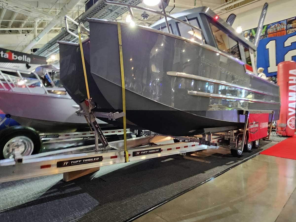 A gray boat on a trailer, displayed indoors with a Yamaha banner and other boats.