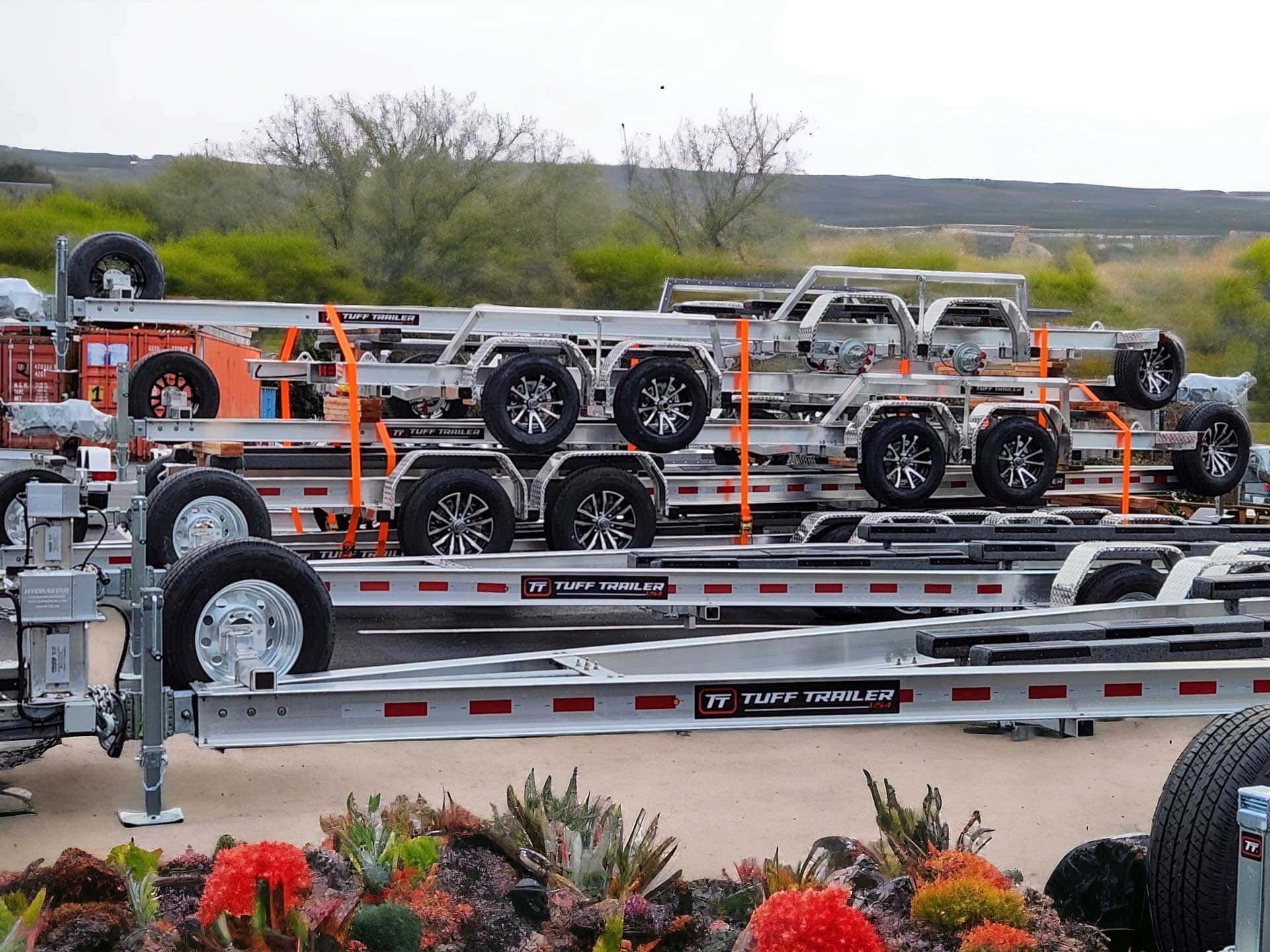 Several stacked, silver car trailers with black tires, outdoors.