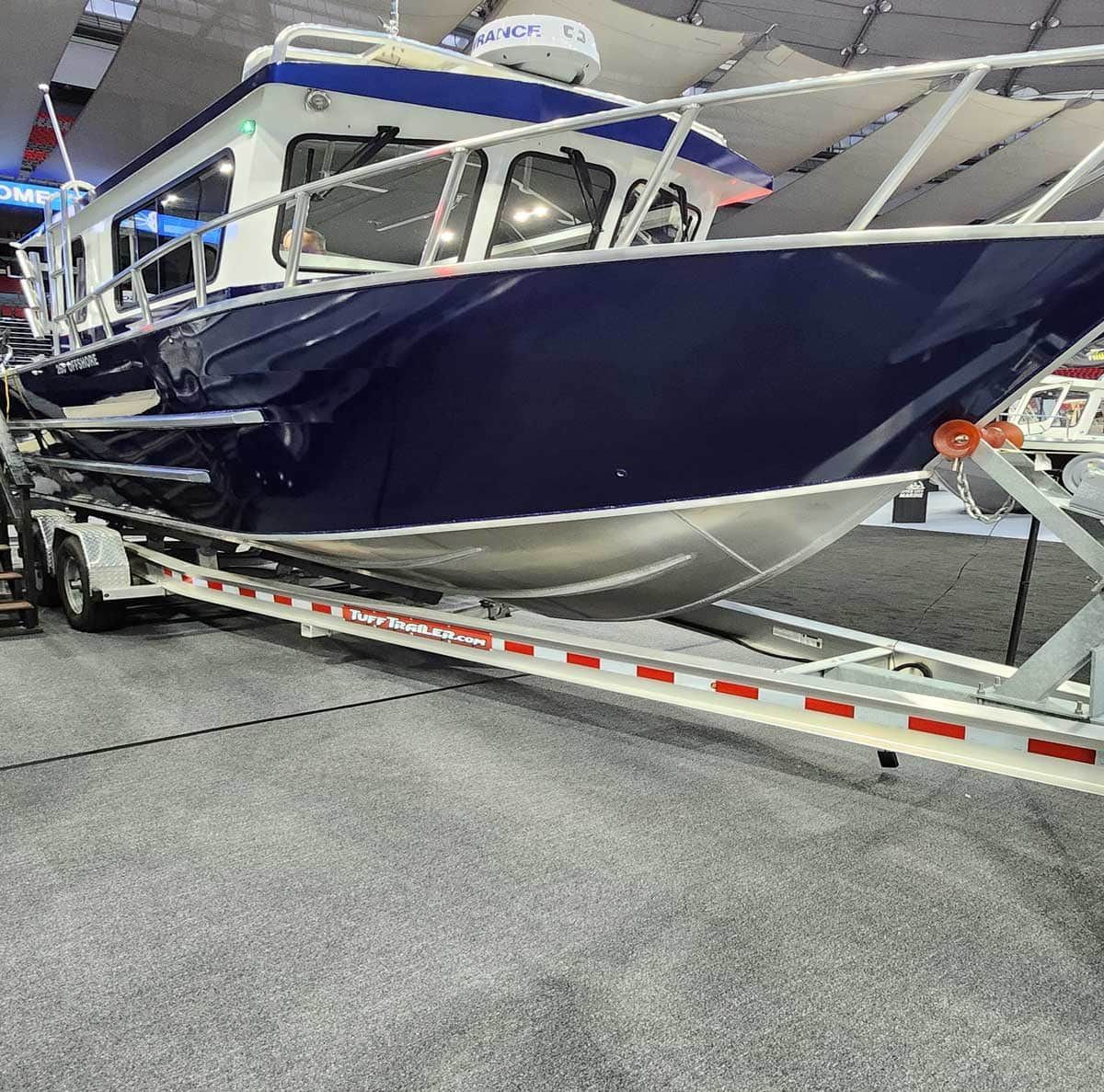 Blue and white boat on a trailer, displayed indoors at a show.