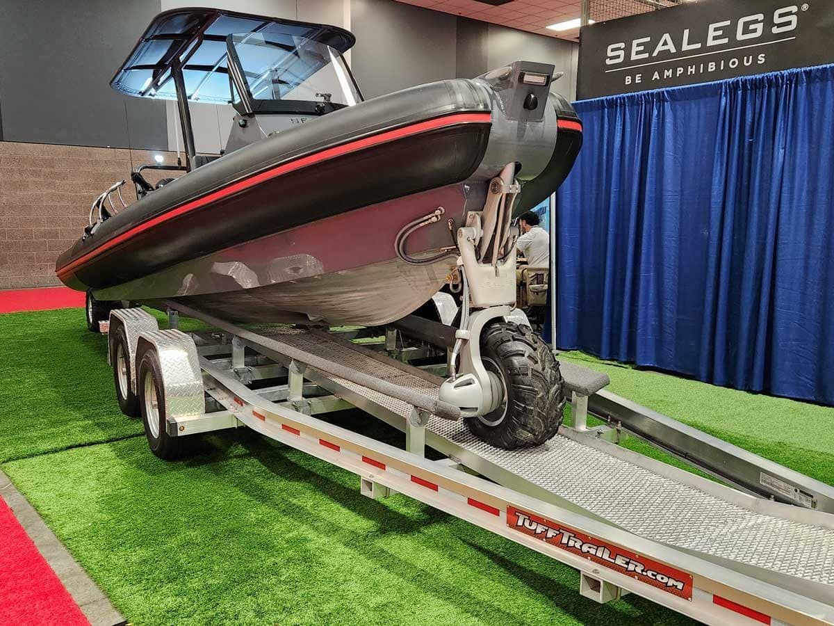 A black Sealegs boat with red trim is on a trailer with wheels lowered; displayed at an event.