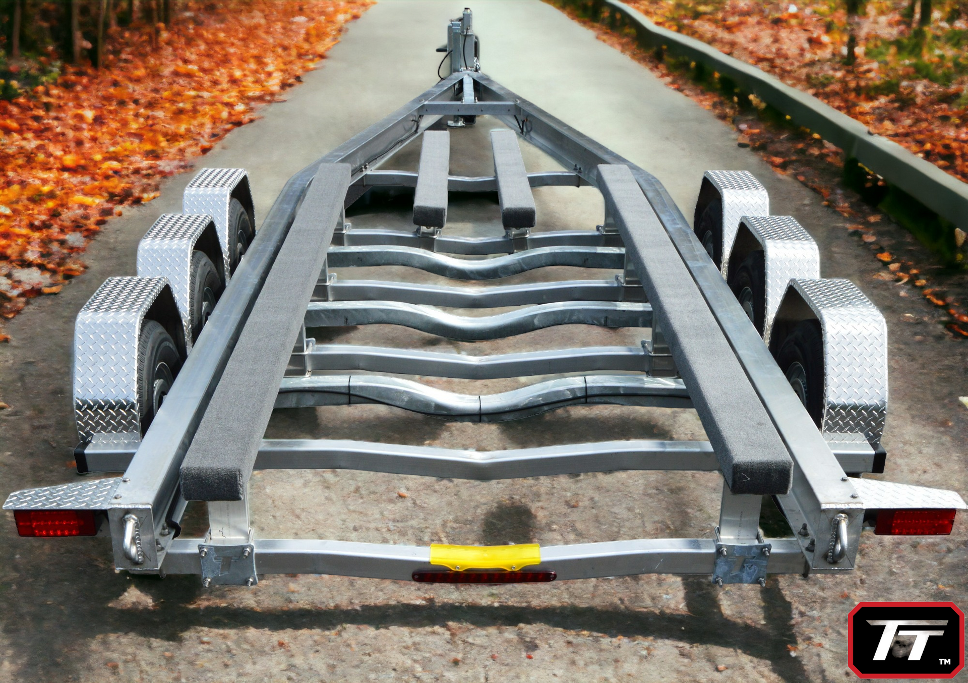 Boat trailer, gray metal frame, on a road. Two axles, red tail lights, autumn leaves.
