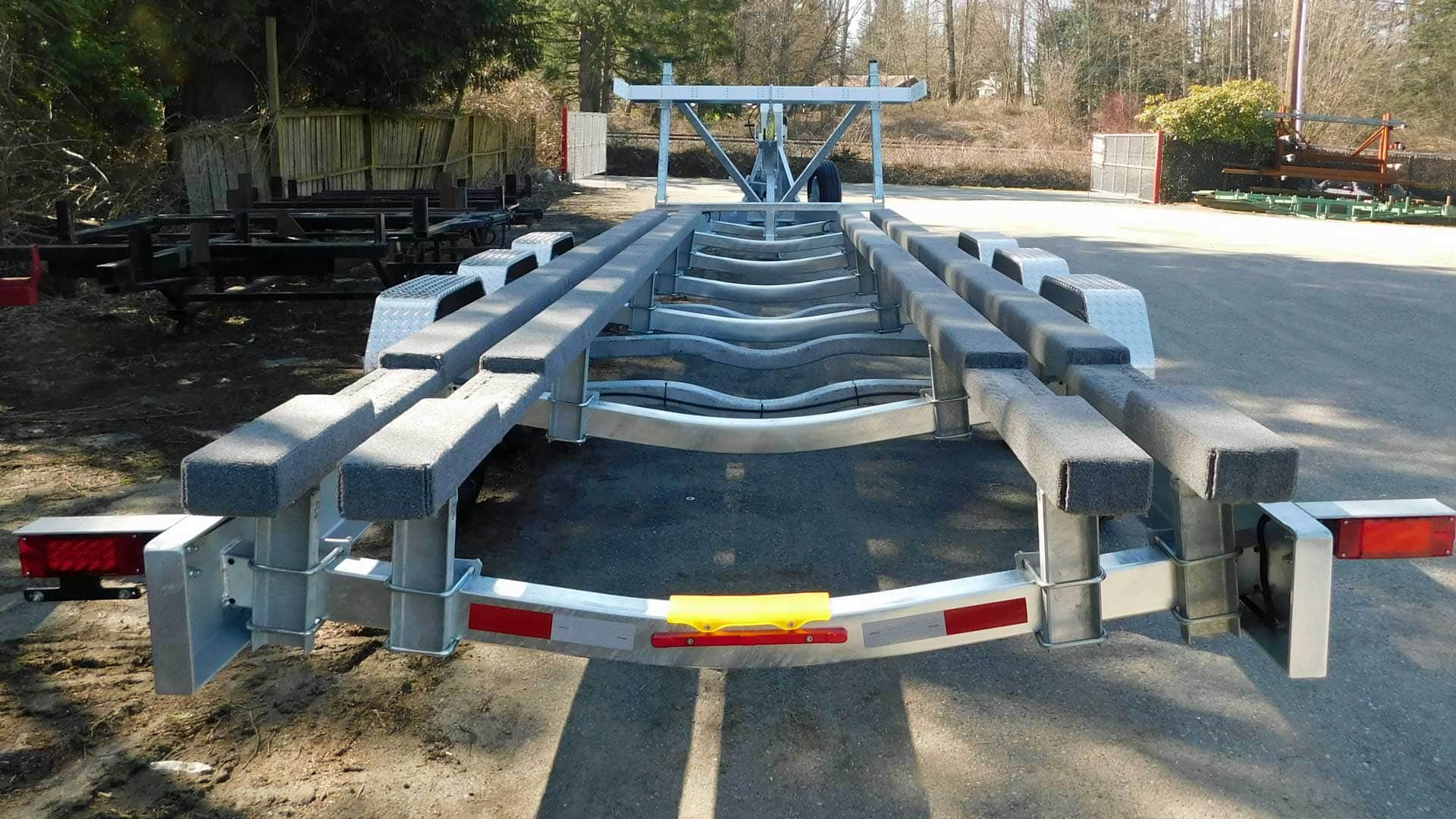 Boat trailer on pavement, with gray metal frame, black supports, and red taillights.