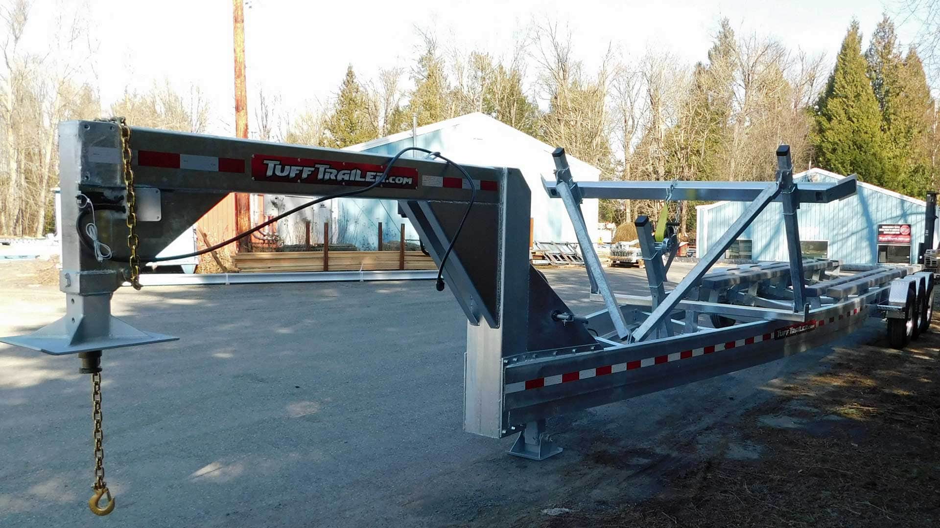 A silver flatbed trailer with a gooseneck hitch. Red and white reflective tape along the side.
