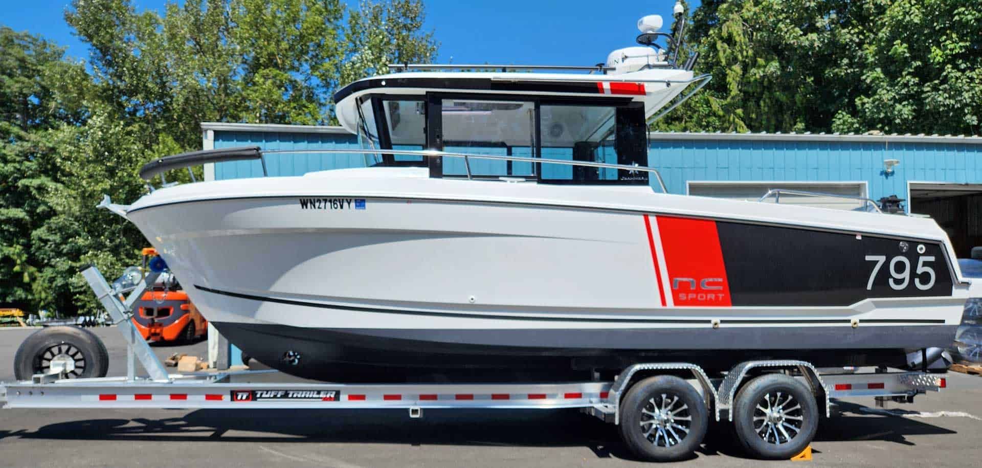 White boat on a trailer, black and red accents, parked in front of a building.