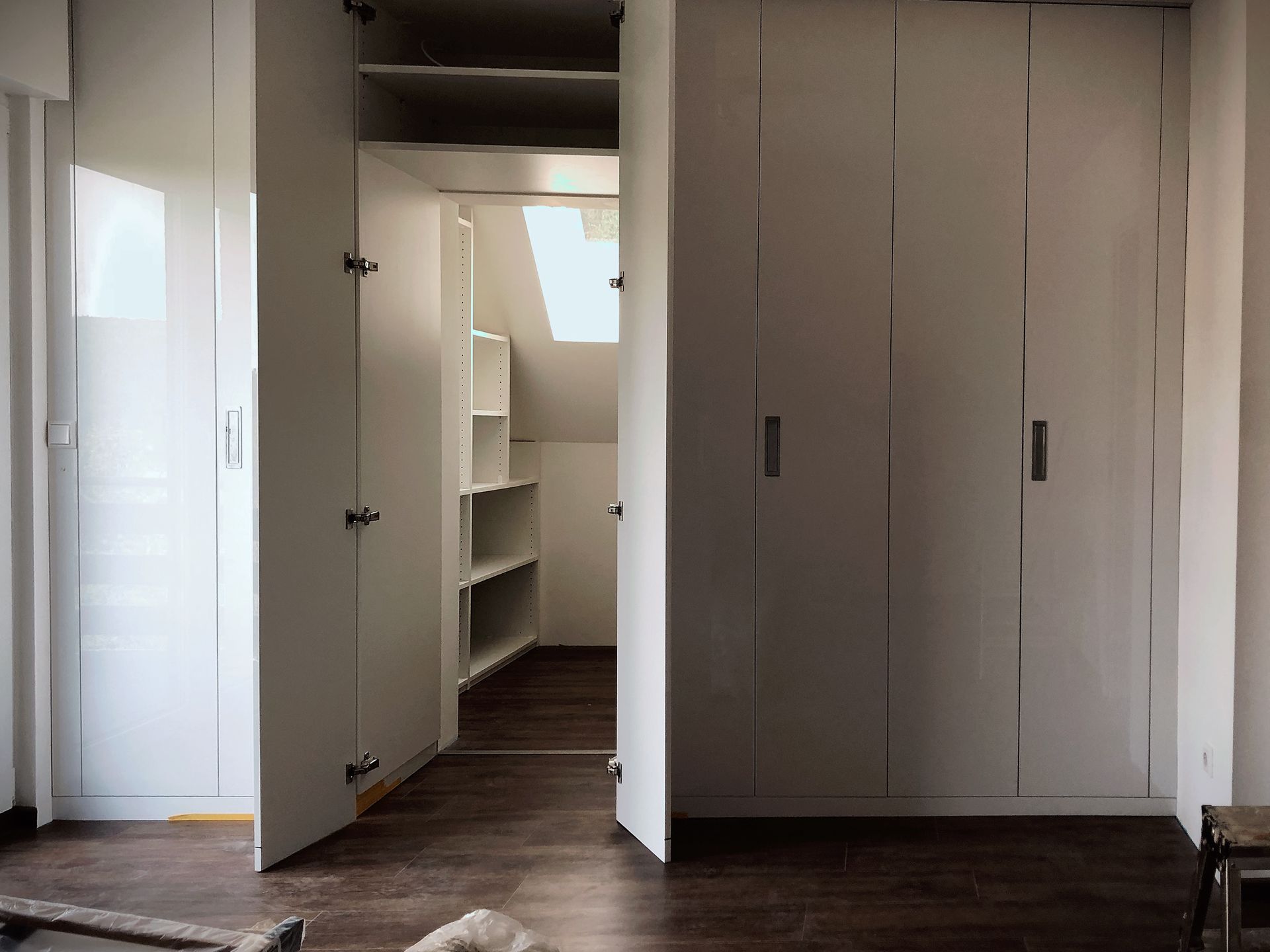 Leerer Flur mit offenen Schranktüren, weißen Wänden und dunklem Holzboden.