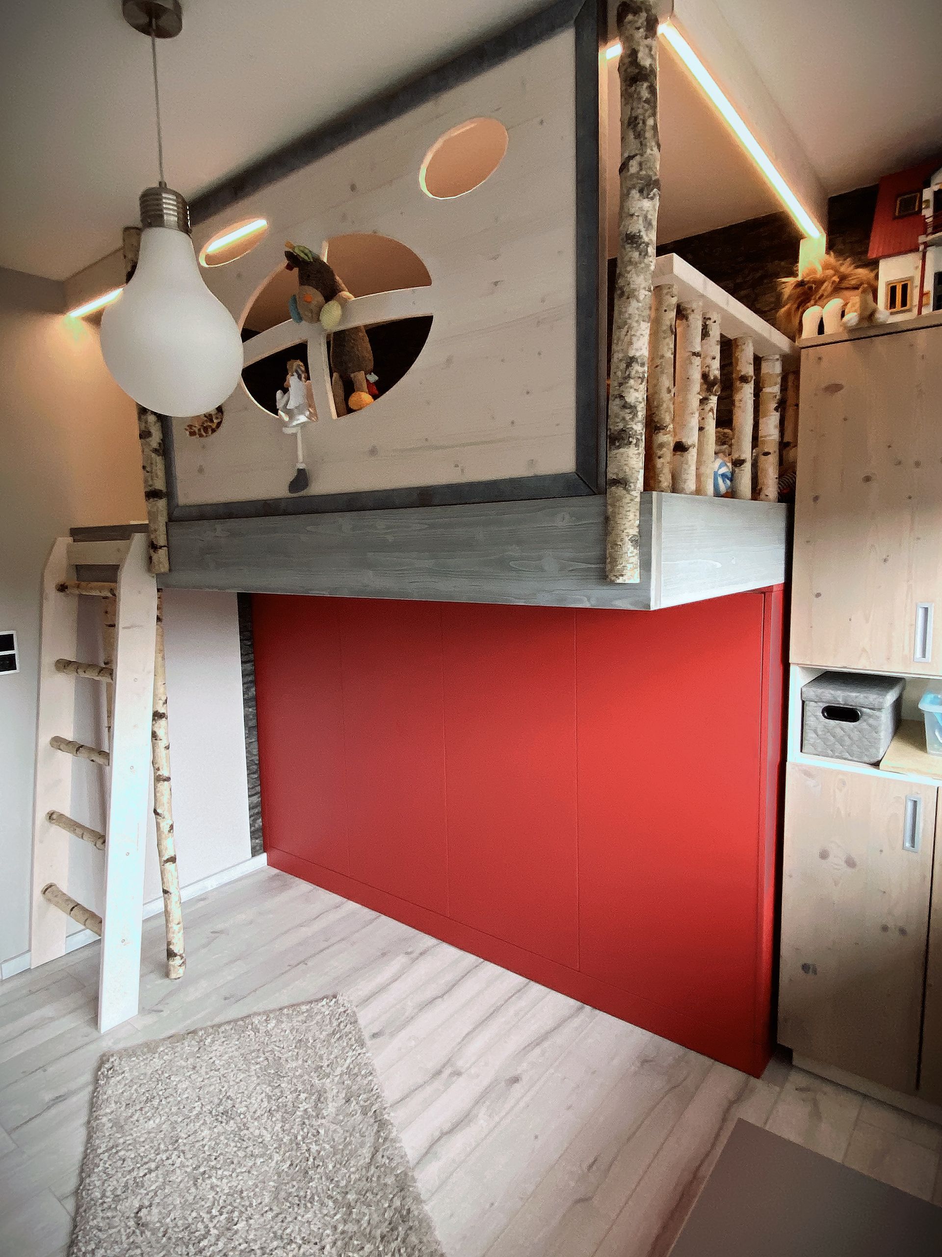 Loftartiger Innenraum mit roter Wand, Leiter, runden Fensterausschnitten und einer Hängelampe