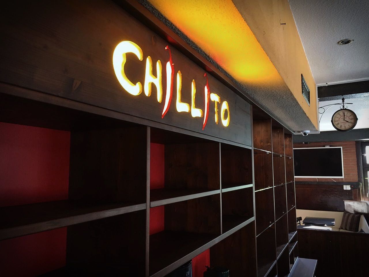 Leeres Restaurantinterieur mit beleuchtetem CHILI-Schild über dunklen Regalen und Sitznischen.