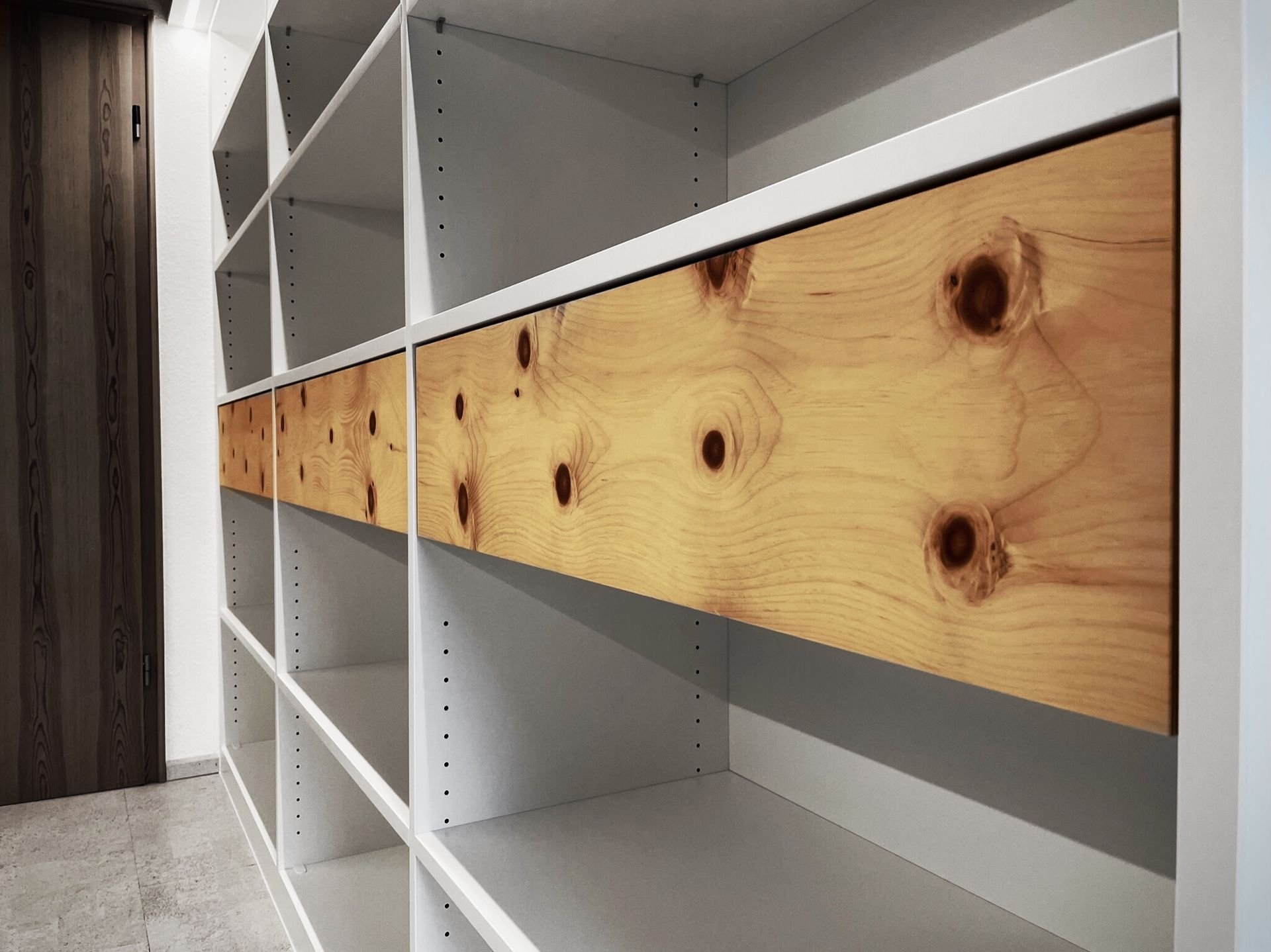 Weißes Regal mit einer horizontalen Holzplanke in der Mitte in einem im Bau befindlichen Raum