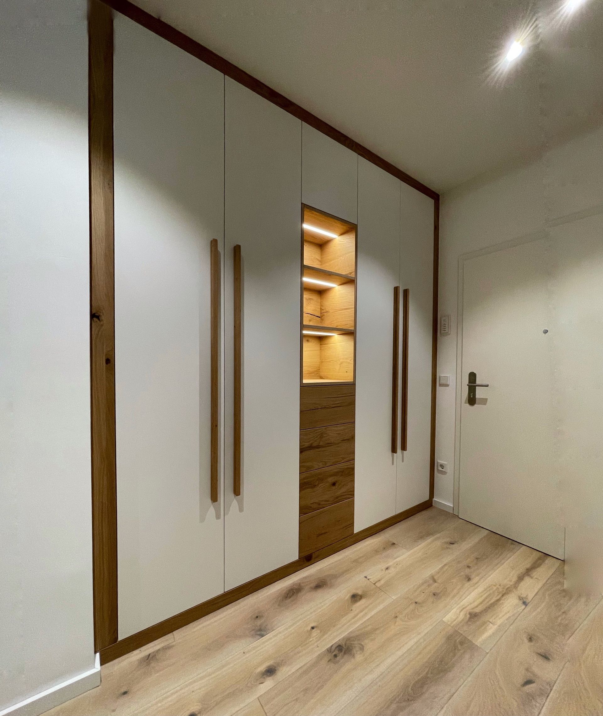 Eingebauter weißer Kleiderschrank mit Holzverkleidung und offenen, beleuchteten Regalen in einem modernen Schlafzimmer