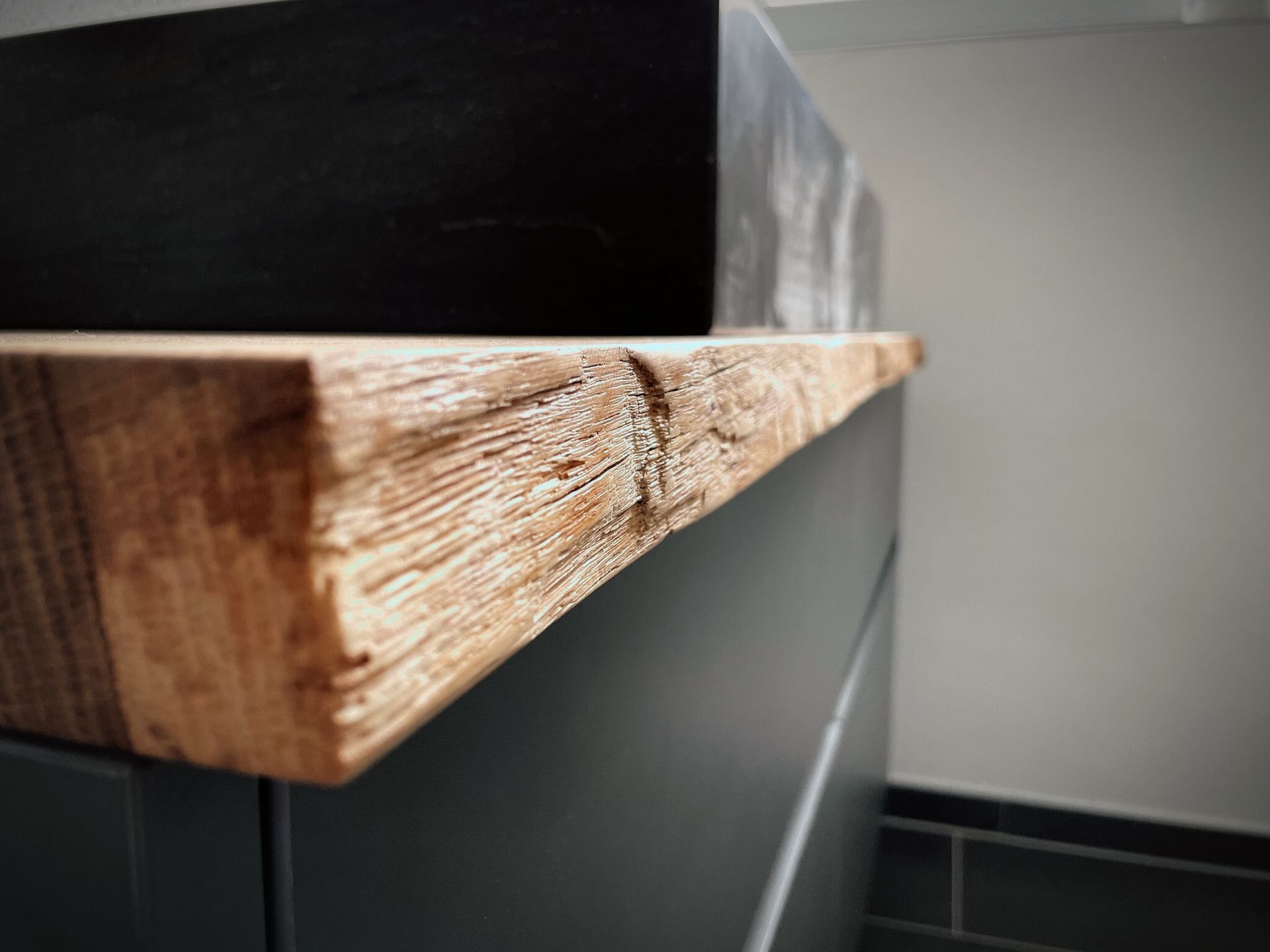 Nahaufnahme einer rauen Holzregalkante vor einem dunklen Schrank und einer grauen Wand