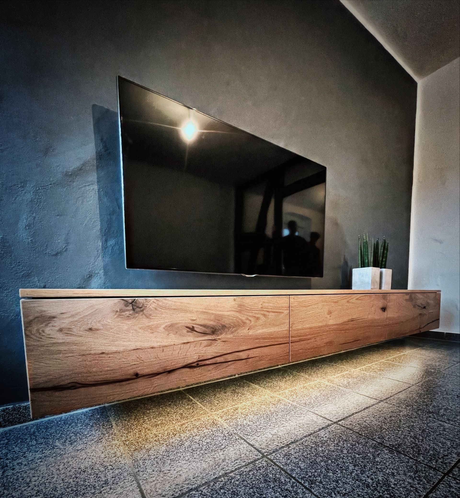 Moderner, an der Wand montierter Fernseher über einem langen Medienschrank aus Holz mit Akzentbeleuchtung in einem schwach beleuchteten Raum