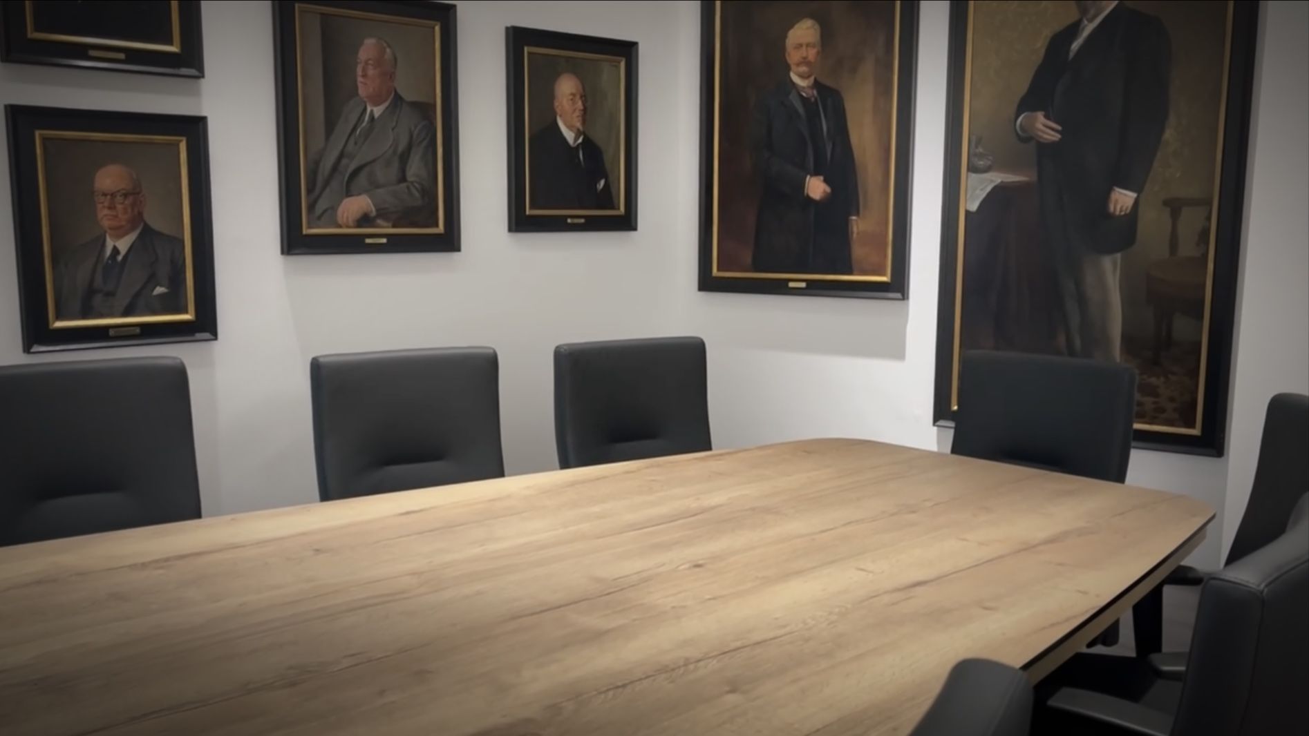 Konferenzraum mit rundem Tisch, schwarzen Stühlen, an der Wand montiertem Fernseher und großen Fenstern.