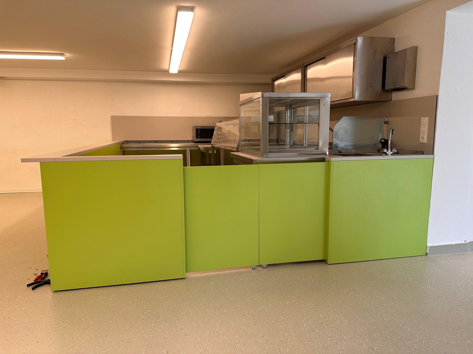 Grüne Kücheninsel mit Glasvitrine in einem Raum unter Neonlicht.