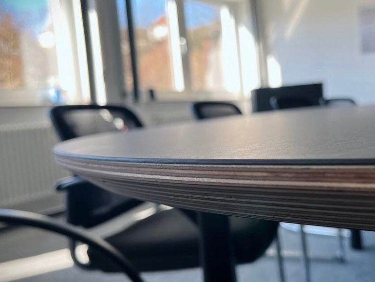 Runder Konferenztisch in einem modernen Besprechungsraum mit Stühlen und großen Fenstern im Hintergrund