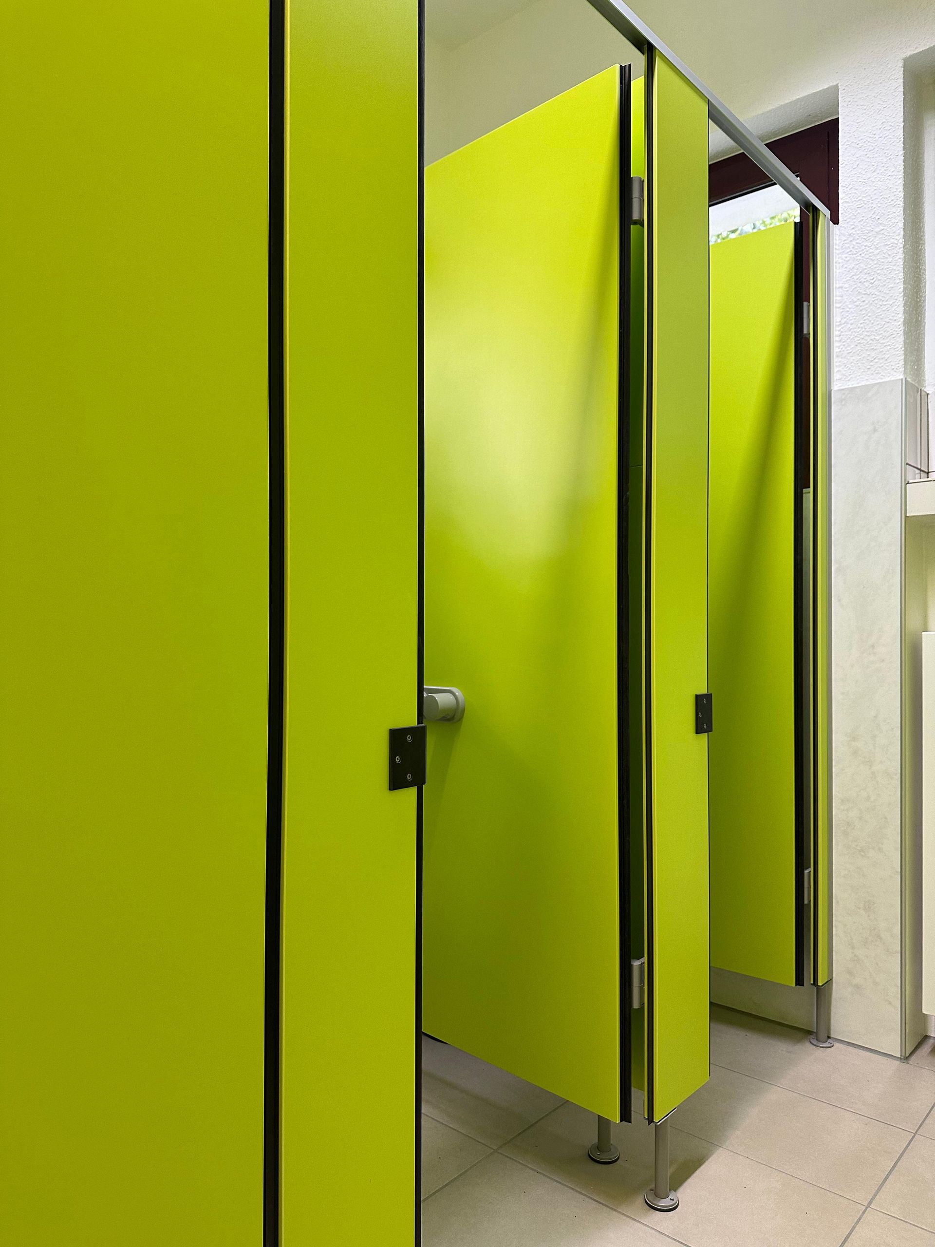 Leuchtend gelbe Toilettenkabinentüren in einer Toilette, eine davon halb geöffnet.